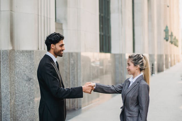 Man in Black Suit Shaking Hands With a Woman in Business Attire